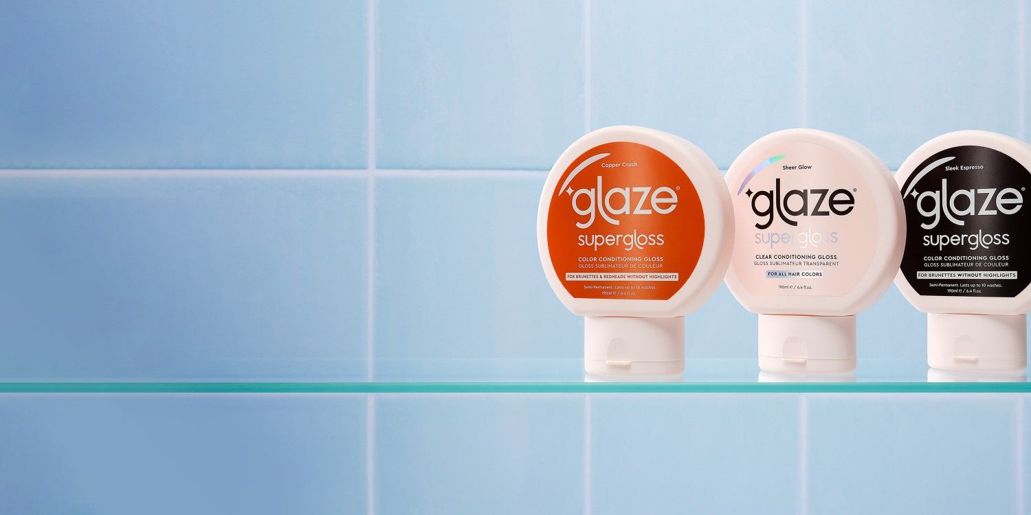 Three bottles of 'glaze supergloss' on a glass shelf against a blue tiled wall.